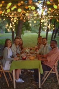 Happy friends sitting by Thanksgiving table and looking at camera outdoors